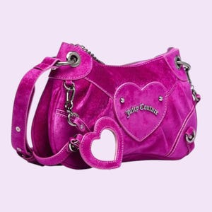 May include: A magenta velvet handbag with a heart-shaped accent and a matching heart-shaped charm. The bag features silver-tone hardware, a shoulder strap, and the text "Juicy Couture" on the heart. The bag has a zip closure.