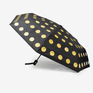 May include: Black umbrella with a repeating pattern of yellow smiley faces. The umbrella is partially open, showcasing its design. The handle is black, and the umbrella appears to be water-resistant, with droplets visible on the surface.