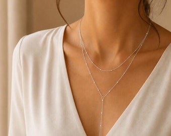 May include: A delicate silver-toned layered necklace featuring two thin chains adorned with small, evenly spaced metallic beads. The design includes a Y-shaped drop element that extends downward from the center of the lower chain.
