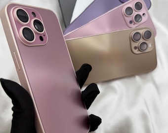 May include: A collection of phone cases in various colors, including mauve, gold, purple, white, and black. The cases have a matte finish and feature a raised camera module. The cases are displayed on a white satin background.