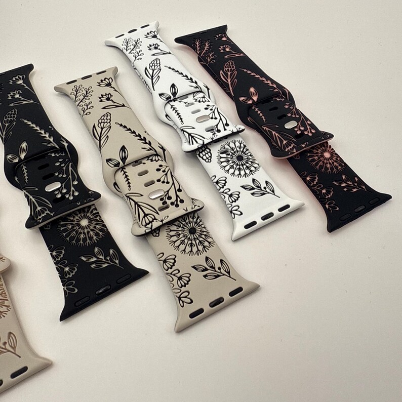 May include: A collection of silicone watch bands featuring botanical line art patterns. The set includes black bands with white floral designs, white bands with black floral prints, beige bands with black floral motifs, and black bands with rose gold floral art.