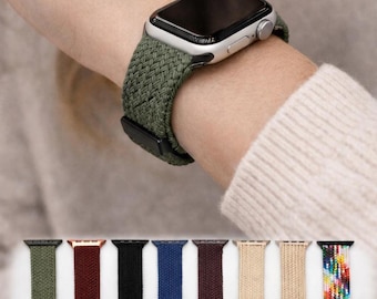 May include: A silver smartwatch with a textured olive green braided nylon watch band. Below, a collection of eight additional watch bands in various colors including olive, maroon, black, blue, dark purple, beige, tan, and a multicolored pattern.