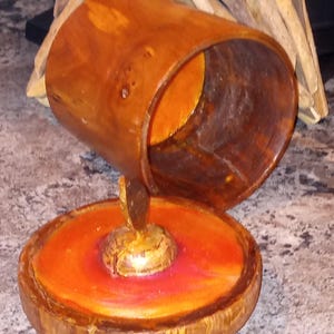 May include: A handcrafted wooden candle holder with a unique design. The candle holder features a cylindrical top and a circular base, both stained in a warm brown hue. The base has an orange and red painted interior, creating a striking contrast.