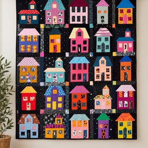 Puede incluir: Un edredón de pared rectangular que presenta una cuadrícula de veinticinco bloques de casas coloridas sobre un fondo negro. Cada casa tiene un diseño único con formas de techo, patrones de ventanas y colores vibrantes variados.
