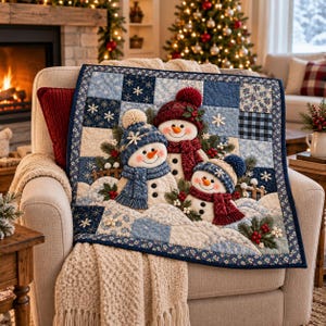 Könnte beinhalten: Ein quadratischer, gesteppter Wandbehang mit dreidimensionalen Stoffschneemännern, die Strickmützen und Schals tragen. Der Quilt besteht aus blau-weißen Patchwork-Quadraten mit Schneeflockenmustern, akzentuiert durch grüne Tannenzweige und rote Beeren.