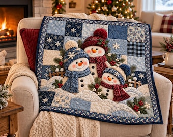 May include: A square quilted wall hanging featuring three dimensional fabric snowmen wearing knit hats and scarves. The quilt is composed of blue and white patchwork squares with snowflake patterns, accented by green pine sprigs and red berries.