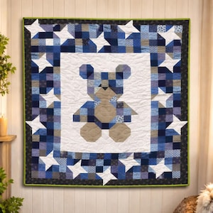 Può includere: Una trapunta fatta a mano con un design a orsetto. La trapunta presenta una figura centrale di orsetto nei toni del blu e del beige, circondata da un bordo di stelle bianche e quadrati blu. La trapunta è rifinita con un bordo verde scuro.