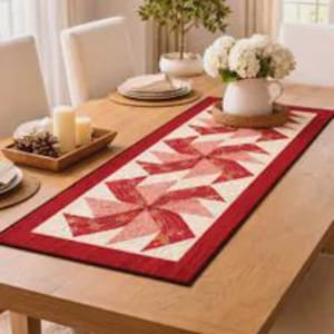 May include: A rectangular fabric table runner featuring a repeating pinwheel quilt pattern in shades of red, pink, and cream. The runner has a solid red border and is centered on a wooden table, showcasing intricate stitching and geometric shapes.
