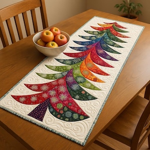 May include: A colorful, quilted table runner in the shape of a Christmas tree. The tree design features a spectrum of colors, including red, orange, green, and blue. The runner is placed on a wooden table, with a bowl of apples nearby.