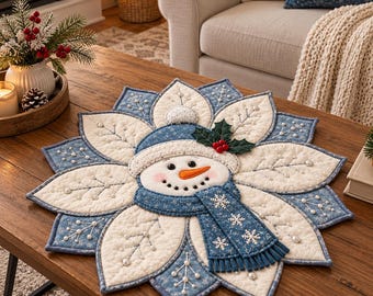 May include: A circular quilted fabric mat featuring a central snowman face with an orange carrot nose, wearing a blue hat and scarf. The mat has white petal-shaped sections decorated with stitched branch patterns and small white beads.