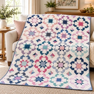 Op de afbeelding: Een patchwork quilt met een herhalend sterpatroon in tinten roze, blauw, paars en groenblauw op een crèmekleurige achtergrond. De quilt is opgebouwd uit diverse stoffen vierkanten en driehoeken, afgewerkt met een donkerblauwe bies.