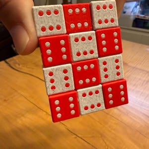 Könnte beinhalten: Ein Würfel-Puzzle aus kleineren Würfeln. Der Würfel besteht aus roten und weißen Würfeln, jeder mit weißen Punkten, die Zahlen darstellen. Die Würfel werden von einer Hand gehalten, mit einer Holzoberfläche im Hintergrund.