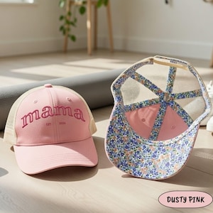 Puede incluir: Gorra de béisbol rosa empolvado con la palabra "mama" bordada en cursiva. La gorra tiene una parte trasera de malla y un interior con estampado floral. El texto "EST 2026" está bordado debajo de "mama".