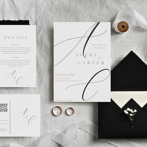 May include: Wedding stationery set including a main invitation with the names "Avery & Carter", RSVP card, details card, and a black envelope. The set includes two gold wedding bands and is decorated with white ribbon and flowers.