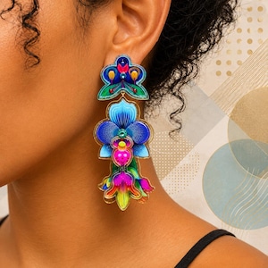May include: A long, multi-layered dangle earring featuring a vibrant floral design. The piece showcases shades of blue, magenta, yellow, and green with intricate line work and small embedded crystals, creating a layered, botanical-inspired aesthetic.