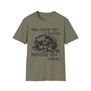 May include: Khaki green t-shirt featuring a black illustration of a 4x4 off-road vehicle on rocks. The text reads "YOU HAVE TO CRAWL BEFORE YOU WALK" above and below the image.