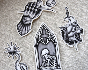 May include: A collection of black and white stickers featuring gothic and medieval designs. Includes a hand in armor holding a tulip, a wolf's head with a sword, a skeleton in a gothic window, and a spiked mace.