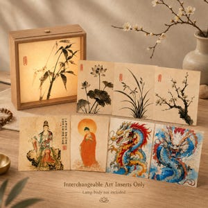 May include: A wooden light box frame with a bamboo print insert, accompanied by seven rectangular art cards featuring ink wash paintings of lotus flowers, orchids, plum blossoms, a deity, a monk, and two colorful dragons with Chinese text.