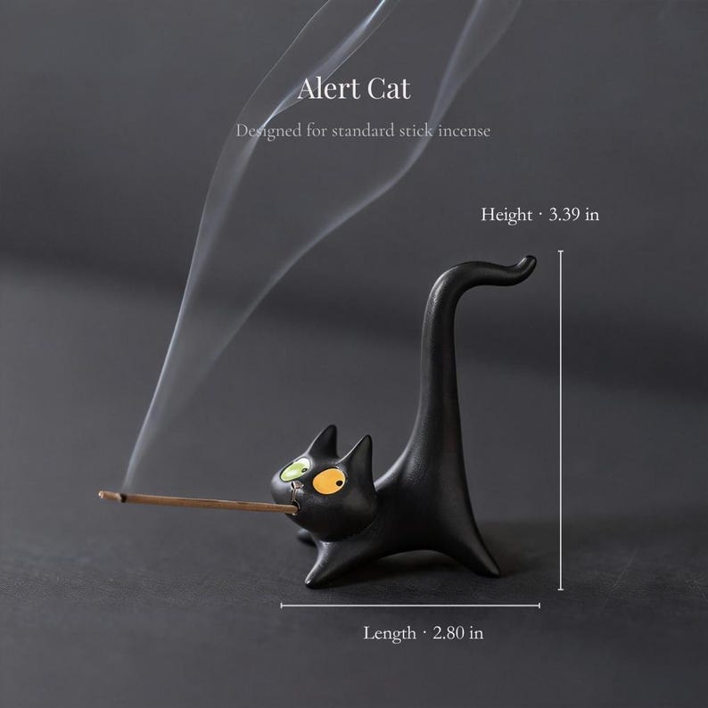 May include: A black cat-shaped incense holder with one green eye and one orange eye, holding a stick of incense in its mouth. The text reads Alert Cat, Designed for standard stick incense, Height 3.39 in, and Length 2.80 in. The cat has a long tail.