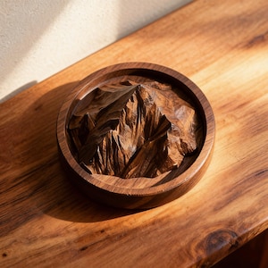 K&ouml;nnte beinhalten: Ein runder Untersetzer aus Holz mit einem geschnitzten Bergketten-Design. Der Untersetzer ist aus dunkelbraunem Holz gefertigt und weist detaillierte Reliefs von Gipfeln und T&auml;lern auf. Er liegt auf einer Holzoberfl&auml;che.