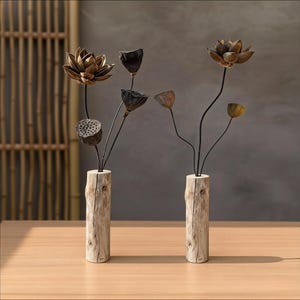 May include: Two decorative floral arrangements with dried lotus flowers and seed pods. The bronze-coloured flowers have dark stems and are set in rustic wooden log vases. The arrangement sits on a light wood table.