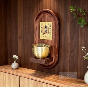 Könnte beinhalten: Eine Wandhalterung aus Holz mit einer Messingschale voller Münzen, vor einem dunklen Holz Hintergrund. Ein kleines Holzregal trägt die Schale, und eine dekorative Tafel mit asiatischen Schriftzeichen befindet sich darüber. Heimdekorations-Thema.