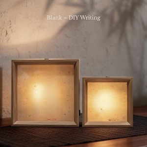 Puede incluir: Dos cajas de luz cuadradas de madera con marcos de color claro y paneles iluminados. El texto "Blank &ndash; DIY Writing" es visible sobre las cajas. Los paneles emiten un brillo c&aacute;lido y suave, y los marcos tienen un acabado de veta de madera natural.