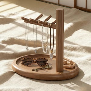 May include: A wooden jewellery organiser with a round base and a vertical post supporting horizontal bars for hanging necklaces. The base holds sunglasses, a key, and a bracelet. The organiser is made of light brown wood.