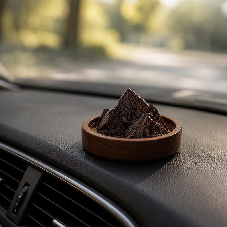 May include: A dark brown wooden circular base containing a sculpted mountain range with jagged peaks and textured slopes. The object is positioned on a black textured surface, featuring a deep brown finish and a realistic, rugged mountain landscape design.