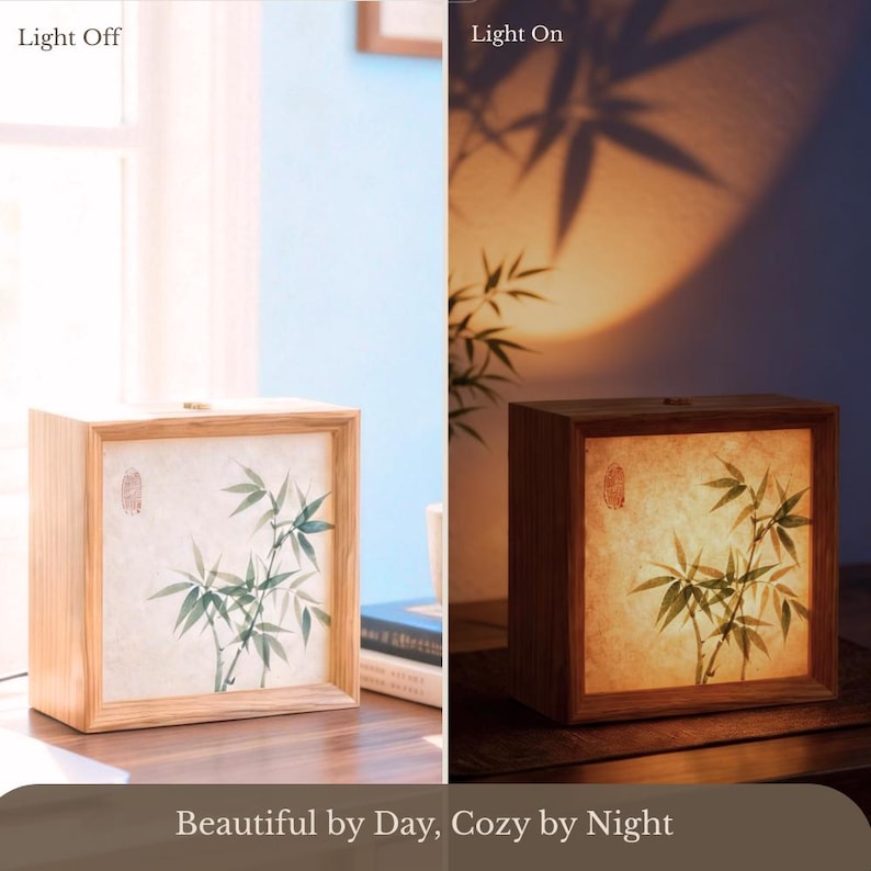 Puede incluir: Una l&aacute;mpara cuadrada de madera con un panel transl&uacute;cido que presenta una ilustraci&oacute;n de bamb&uacute; verde y un sello rojo. La imagen muestra dos estados: Luz apagada con panel blanco y Luz encendida con una c&aacute;lida iluminaci&oacute;n &aacute;mbar.