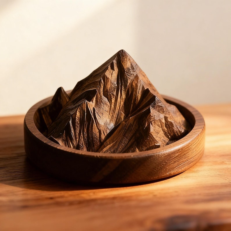 K&ouml;nnte beinhalten: Eine handgeschnitzte Holzskulptur eines Bergmassivs. Die dunkelbraunen Berge sind detailliert geschnitzt und in einer kreisf&ouml;rmigen Holzbasis platziert. Die Skulptur wird auf einer Holzoberfl&auml;che pr&auml;sentiert, die die nat&uuml;rliche Holzmaserung hervorhebt.