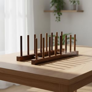 Puede incluir: Un escurridor de platos de madera marrón oscuro con dos bases rectangulares paralelas conectadas por una varilla horizontal, con múltiples clavijas verticales que se extienden hacia arriba para sostener platos. El nombre Zenboodi está impreso en el lateral.