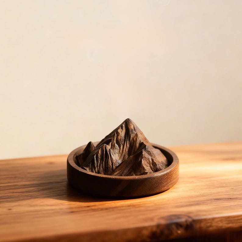 K&ouml;nnte beinhalten: Eine Holzskulptur eines Berges in einer runden, dunkelbraunen Holzschale. Der Berg hat detaillierte Grate und Gipfel, und die Schale steht auf einer Holzoberfl&auml;che. Die Skulptur ist ein dekorativer Gegenstand.