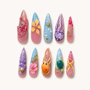 May include: A set of ten stiletto-shaped press-on nails featuring ocean-themed 3D designs. The nails display various motifs including a pink crab, yellow flowers, bubbles, a purple jellyfish, a seashell, an octopus, a sea turtle, and a starfish.