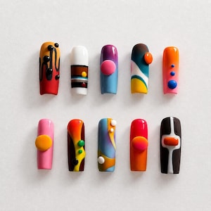 May include: Ten artificial nails with diverse designs are displayed. The nails showcase a spectrum of colours, such as red, pink, blue, and orange, with abstract patterns and embellishments like dots and circles. Each nail has a unique design.