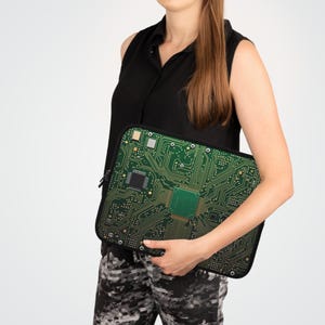 May include: A black laptop sleeve featuring a green circuit board design. The sleeve has a black zipper and is held by a person. The circuit board design has a complex pattern of lines and squares.