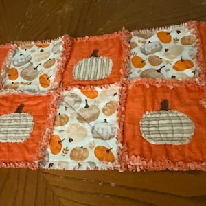 Pode incluir: Um caminho de mesa tipo rag quilt com um design de patchwork de quadrados laranja s&oacute;lidos alternados com quadrados brancos estampados com v&aacute;rias ab&oacute;boras. As bordas de cada quadrado s&atilde;o desfiadas, criando uma apar&ecirc;ncia texturizada.