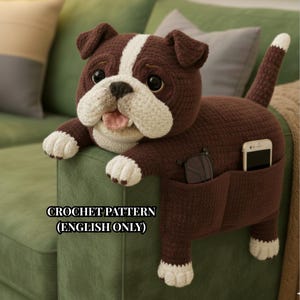 May include: A brown and white crochet bulldog-shaped sofa arm organizer. The dog has a white stripe on its head, white paws, and a pocket for a phone and glasses. The text "CROCHET PATTERN (ENGLISH ONLY)" is visible.