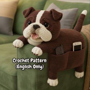 Puede incluir: Un organizador de sofá con forma de bulldog tejido a ganchillo en marrón y blanco, con bolsillos para gafas y teléfono. El perro tiene una raya blanca en la cabeza y patas blancas. El texto "Crochet Pattern (English Only)" es visible.