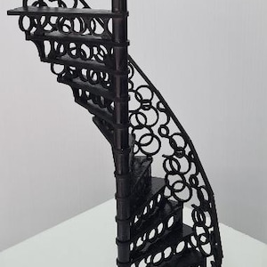 Könnte beinhalten: Schwarzes Metall-Wendeltreppenregal mit dekorativen kreisförmigen Ausschnitten. Das Regal hat einen halbkreisförmigen Sockel und eine zentrale Stützsäule. Die Stufen und das Geländer weisen ein sich wiederholendes Kreisdesign auf.