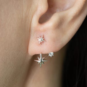May include: Close-up of three earrings on an ear. The earrings include two silver starburst studs and a small, round, clear gemstone stud. The starburst studs have multiple points and a shiny finish.