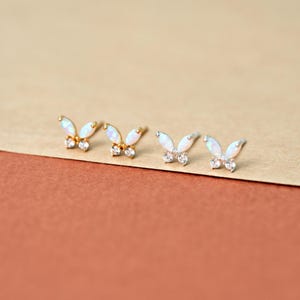 May include: Four butterfly-shaped stud earrings arranged in a row. Each earring features two marquise-cut white opal wings and two small clear round stones at the base. Two earrings are set in gold-tone metal, and two are set in silver-tone metal.