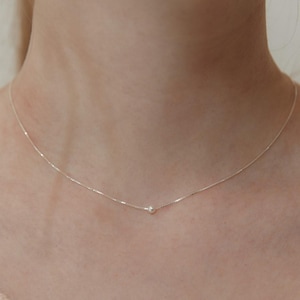 May include: A fine silver necklace with a single, small pearl pendant. The chain is delicate. The necklace is shown against a neutral background, emphasising its minimalist design. The pearl is approximately 0.3 cm in diameter.