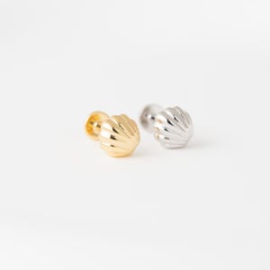 May include: A pair of stud earrings shaped like seashells, featuring one gold-toned metal earring and one silver-toned metal earring. Each earring has a rounded, ribbed surface texture and a post back mechanism for secure attachment.