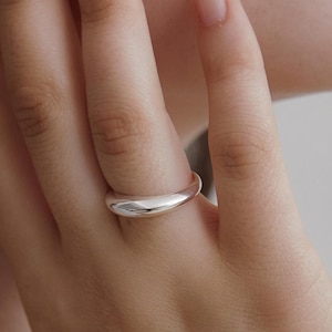 Puede incluir: Un anillo de tono plateado, liso y pulido, con una banda gruesa y redondeada. El anillo presenta una construcción de metal sólido y continuo con una superficie reflectante de alto brillo que se curva suavemente alrededor del dedo.