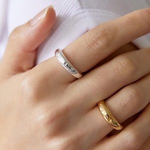 Könnte beinhalten: Zwei Ringe, einer silberfarben und einer goldfarben, werden gezeigt. Der silberne Ring hat ein Sternmuster. Der goldene Ring hat ebenfalls ein Sternmuster. Die Ringe befinden sich an den Fingern einer Person.