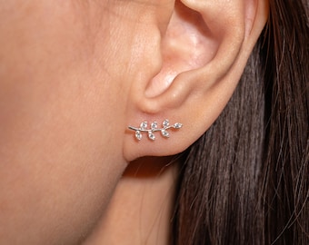 May include: A silver-toned ear climber earring shaped like a delicate branch with five small, clear, marquise-cut stones set along the stem. The earring follows the curve of the earlobe, featuring a metallic finish and sparkling white accents.