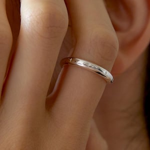 Puede incluir: Un anillo plateado pulido con grabados en forma de estrella. El anillo se lleva en un dedo, con el tono de piel visible en el fondo. El diseño del anillo es simple y elegante.