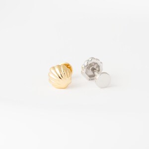 May include: A pair of stud earrings featuring a gold-toned shell-shaped front and a silver-toned flat circular backing. The shell design has vertical ridges and a polished finish, while the post mechanism is visible on the second earring.