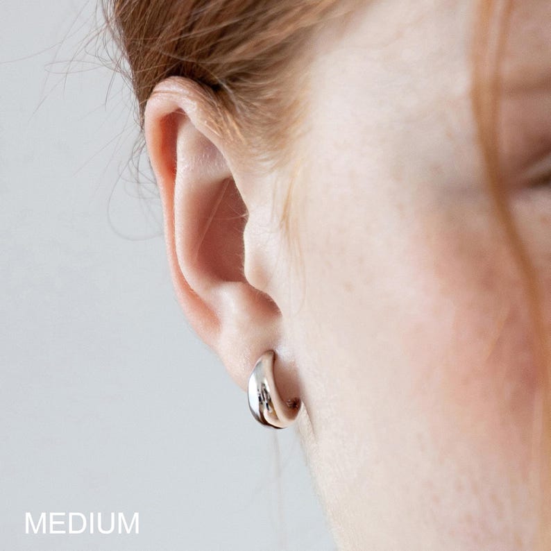 May include: A close-up of a silver hoop earring. The earring is a medium size and is worn on an ear. The word "MEDIUM" is printed in white at the bottom of the image.